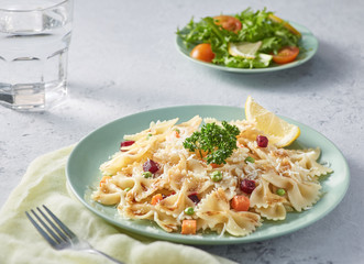Butter and farfalle with colorful vegetables. Homecook. With grey color texture background and harsh light. Front view.