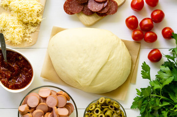 Yeast dough with prepared pizza ingredients on a white wooden background