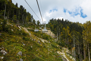 Cable car at a ski resort in summer. Forest, mountains and blue cloudy sky. Hemp of felled trees.