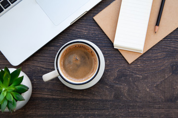 Wooden desk table with computer, notebook and hot coffee
