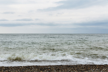 Skyline on the black sea in the city of Sochi. The photo shows a pebble beach, waves on the sea and a blue cloudy sky.