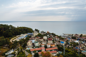 View of a small resort town near the city of Sochi. The photo shows the Black Sea, small hotels, residential buildings, green trees and blue sky.