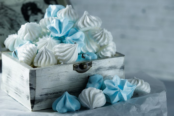 white and blue meringues in the form of drops, lies in a wooden box on a table on paper, against a background of a brick wall