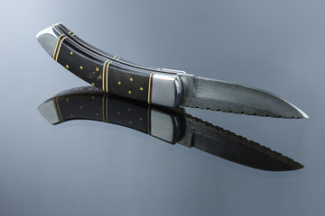 folding pocket knife on a mirrored surface, blade made of multi-layer Damascus steel, handle made...