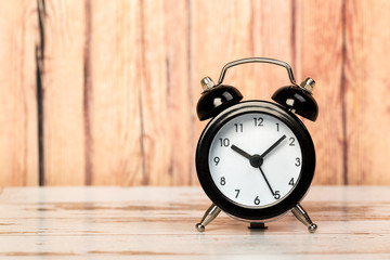 Black retro alarm clock with bells on a wooden table, daily routine concept.