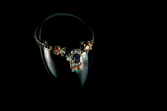 A necklace made by hand in an unusual way is presented of a portrait mannequin woman. On a dark background and highlighted at the back, the necklace glitters. Reflections. Not precious stones or metal