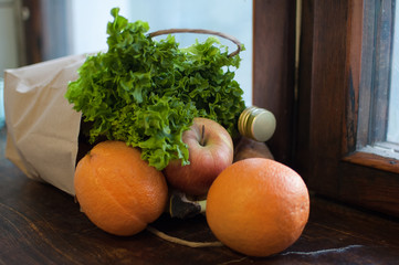 Product set, green salad and fruits are lying on the wooden windowsill in craft paper package. Delivery food, proper nutrition concept