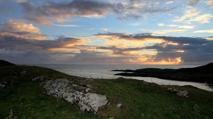 Dramatischer Sonnenuntergang über dem Meer mit Felsen und Landzunge im Vordergrund