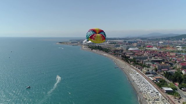 From great height best color parachute parasailing people fly. Modern cityscape Sochi Russia. Blue sea ocean coastal popular beach attraction. Activities entertainment extreme. Summer