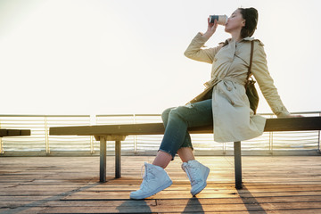 Young cute girl seating at the seafront and drinking her morning coffee in profile