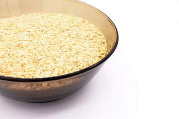 A dark glass plate is filled with long-grain brown rice on a white background. Close up.