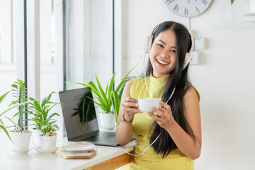 Asian smiling girl student wear wireless headphone study online with skype teacher in a coffee...