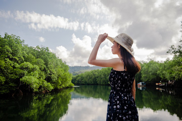 Asian women standing, wearing a hat and admiring the River view with mangrove forest. And the clear skies with beautiful clouds. Suitable for tourism, recreation and relax