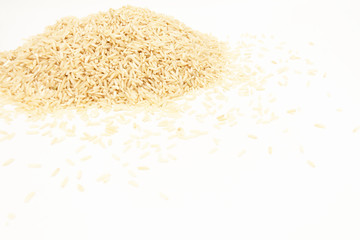 A pile of long-grain, brown rice on a white background lies in the upper-left corner. Side view with space for text.