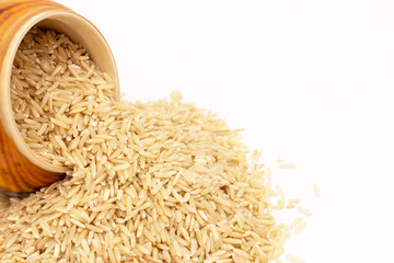 Крупный план перевернутого деревянного горшка из которого высыпался длиннозерный коричневый рис на белый стол. 