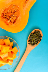 Half a pumpkin, fresh slices in a bowl and pumpkin seeds in a wooden spoon on a blue background. Natural food. Suitable for background. Vegan. Cooking dish from vegetable ingredient, plant-based food.
