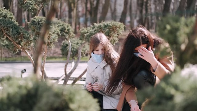 European mother and her daughter are walking with a dog. It's quarantine period so the mother and her child are wearing disposable masks to protect themselves from virus. The parent and chils are