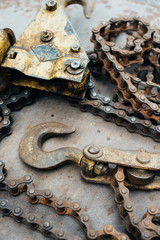 Old rusty soviet homemade winch, with traces of yellow paint. Hook, bicycle chain, chain links. The winch lies on a sheet of rusty iron. Scrap metal. Close-up. Macro