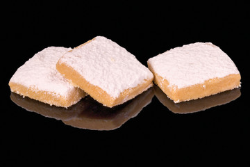 Three cookies with butter and sugar powder, isolated on black background, with reflection