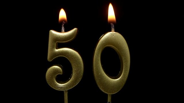 Burning golden birthday candles on black background, number 50