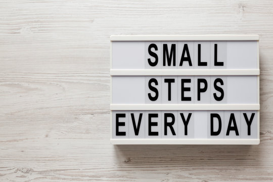 'Small steps every day' words on a modern board on a white wooden background, top view. Overhead, from above, flat lay. Copy space.