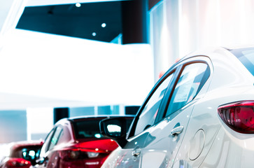 Rear view of white luxury car parked in modern showroom for sale. White shiny car on blurred red...