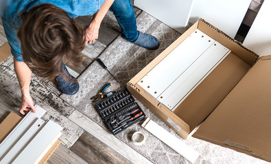 Young man unpacking box with DIY furniture for home