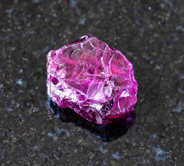 Fototapeta premium closeup of sample of natural mineral from geological collection - rough Rhodolite (pyrope garnet) crystal on black granite background from Lokirima, Lodwar, Turkana dist, Riffvalley prov, Kenya