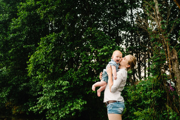 Young mother kissing baby girl walk in park. Family holiday in garden. Portrait mom with child together on nature. Mum, little daughter outdoors. Happy Mothers Day. Close up.