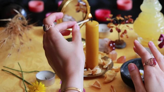 A witch (wearing some vintage jewelry) lighting a yellow candle on her Litha midsummer Sabbat Solstice celebration altar filled with flowers and random things corresponding to the Sun. Unedited
