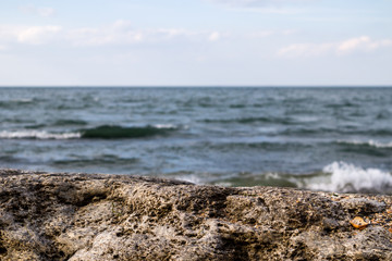 Fototapeta na wymiar Sea waves with large coastal rocks on background. Clean, blue sky with clouds.