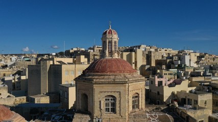 Aerial view of dome of the church against the backdrop of the city, historical architecture. Roof tops. Bormla, Valletta, Malta. Travel destinations. European culture and religion.
