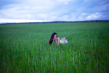 Alone pretty woman lies in the field of green grass in overcast sky . Young happy girl dressed maxi dress enjoy the freedom of the meadow