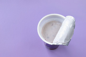 A pink yogurt with strawberry in an open plastic cup on pink background.