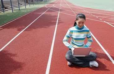 Girl sitting on the sports track using laptop.