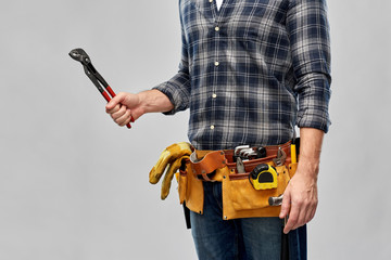 repair, construction and building - male worker or builder with adjustable wrench and working tools on belt over grey background