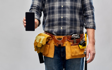 repair, construction and building - male worker or builder with smartphone and working tools on belt over grey background