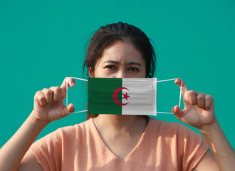 A woman with Algeria flag on hygienic mask in her hand and lifted up the front face on green background. Tiny Particle or virus corona or Covid 19 protection.
