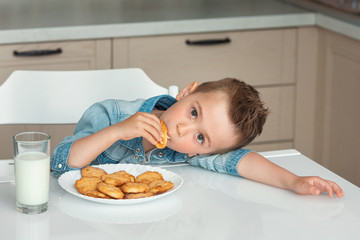 Cute little boy eats cookies with milk