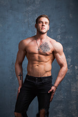 Fototapeta premium Pionowe ujęcie muskularnego mężczyzny z nagim torsem. Model fitness w dżinsach na szarym tle.