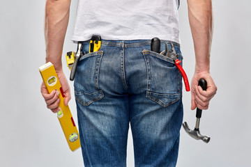 repair, construction and building - male worker or builder with level and working tools in back pockets over grey background