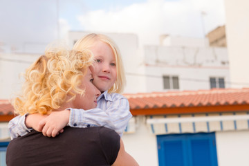 Mother and son children hug and love together with happiness - back view of young mummy and little child have fun with city houses in background - caucasian family concept