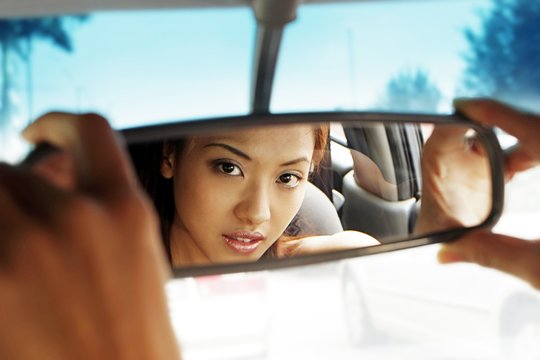 Mirror reflection of woman adjusting the rear view mirror of car.