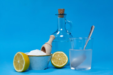 natural cleaning stuff, sustainability and eco living concept - lemon halves, washing soda, bottle of vinegar and glass with spoon over blue background