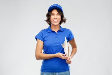 mail service and shipment concept - happy smiling delivery girl in blue uniform with clipboard over grey background