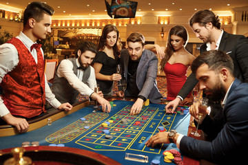 Friends make bets gambiling at the roulette table in the casino.