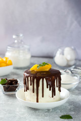 A white cake on the table covered in chocolate with sliced peaches on top is on the white table in the kitchen. The ingredients for making the cake are next to each other