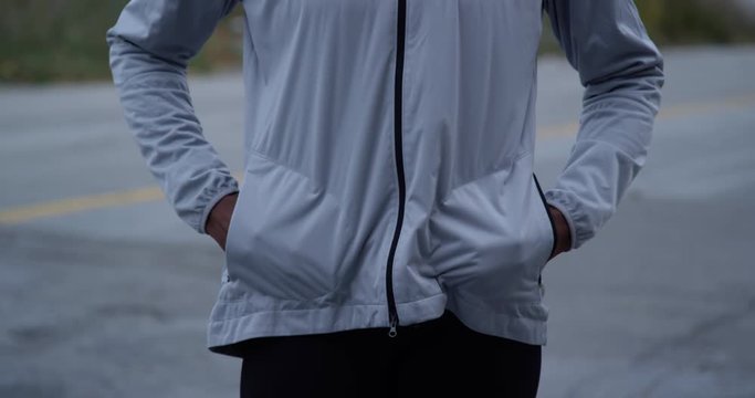 Woman jogger athlete unzips her running jacket and puts her hands in her pockets due to cold weather