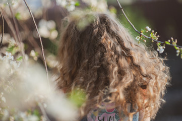 Cute little girl with curly hair in a flowering garden