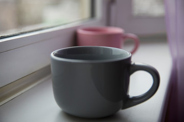 Obraz premium Two empty ceramic mugs of gray and pink on the windowsill.